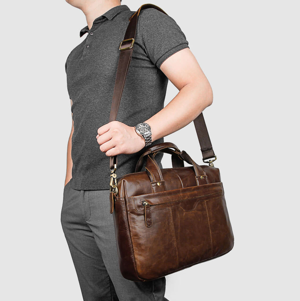 Lifestyle shot of man using vintage brown leather laptop bag outdoors.