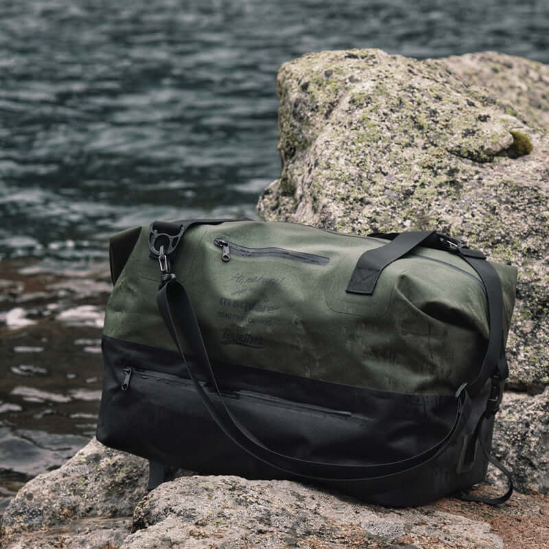 Waterproof duffle bag placed on rocky terrain near a river.