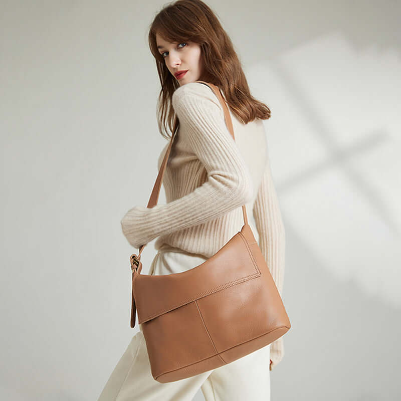 Model carrying a brown leather crossbody bag as a shoulder bag.